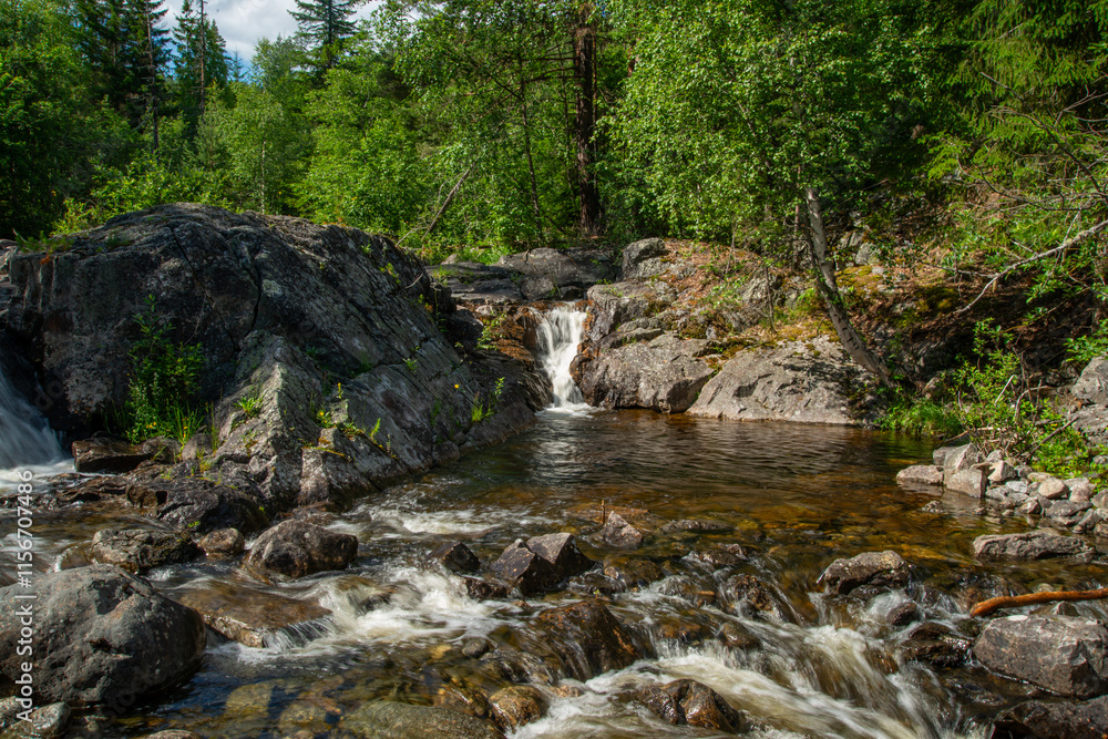 Norwegian mountain river with fast flowing clear and sparkling water and a waterfall that forms white foam on rocks surrounded by green coniferous trees. Sunny summer day. Norwegian mountain river with fast flowing clear and sparkling water and a waterfall that forms white foam on rocks surrounded by green coniferous trees. Sunny summer day.