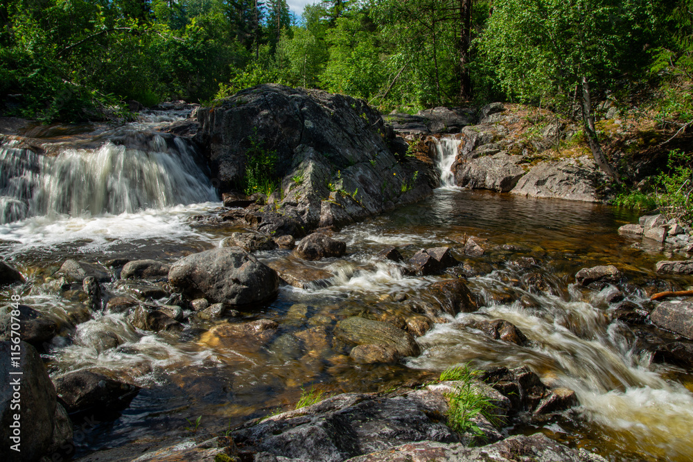 Norwegian mountain river with fast flowing clear and sparkling water and a waterfall that forms white foam on rocks surrounded by green coniferous trees. Sunny summer day. Norwegian mountain river with fast flowing clear and sparkling water and a waterfall that forms white foam on rocks surrounded by green coniferous trees. Sunny summer day.
