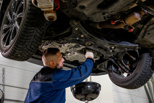 A working car mechanic unscrews the drain plug of the crankcase on the pallet to drain and replace the engine oil