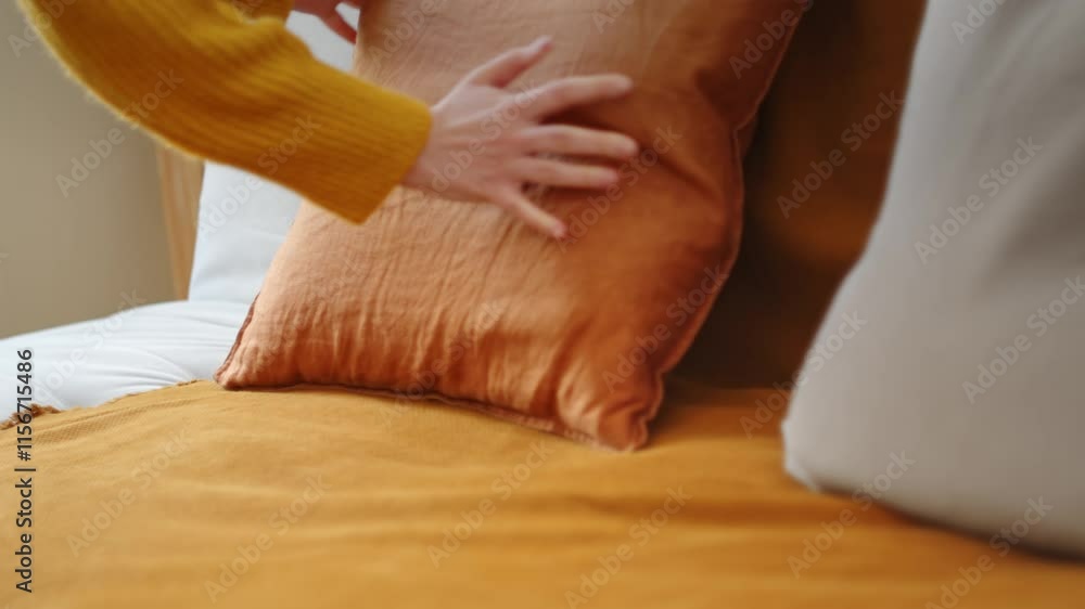 Person arranging an orange pillow on a matching sofa for a cozy living room setting Person arranging an orange pillow on a matching sofa for a cozy living room setting