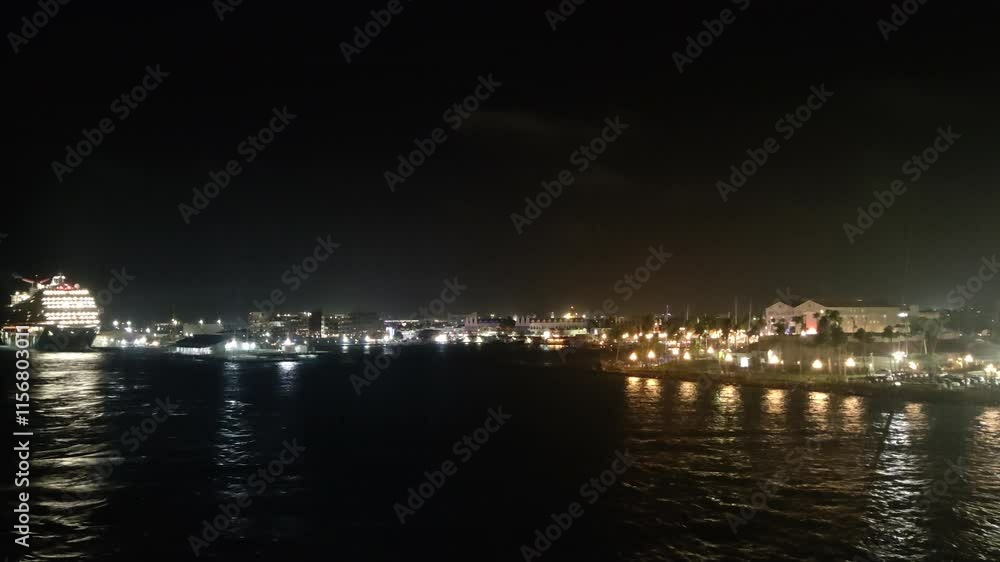 Large, brightly lit cruise ship departs from aruba at night, leaving behind an illuminated pier and the twinkling lights of the city skyline Large, brightly lit cruise ship departs from aruba at night, leaving behind an illuminated pier and the twinkling lights of the city skyline