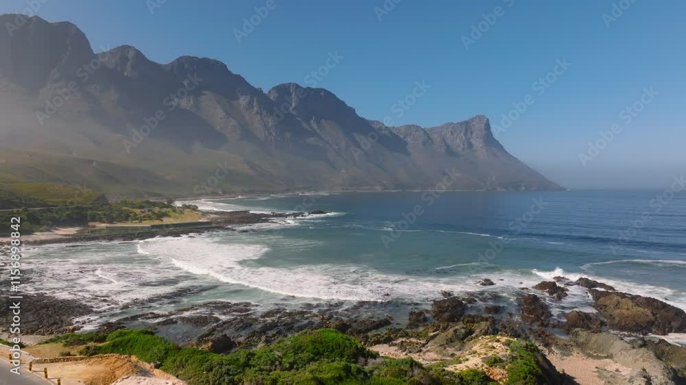 Aerial approaching shot of Koeel Bay Surfer Spot in Cape Town. Waves reaching shore during foggy day in South Africa. Mountain range in distance. Aerial approaching shot of Koeel Bay Surfer Spot in Cape Town. Waves reaching shore during foggy day in South Africa. Mountain range in distance.
