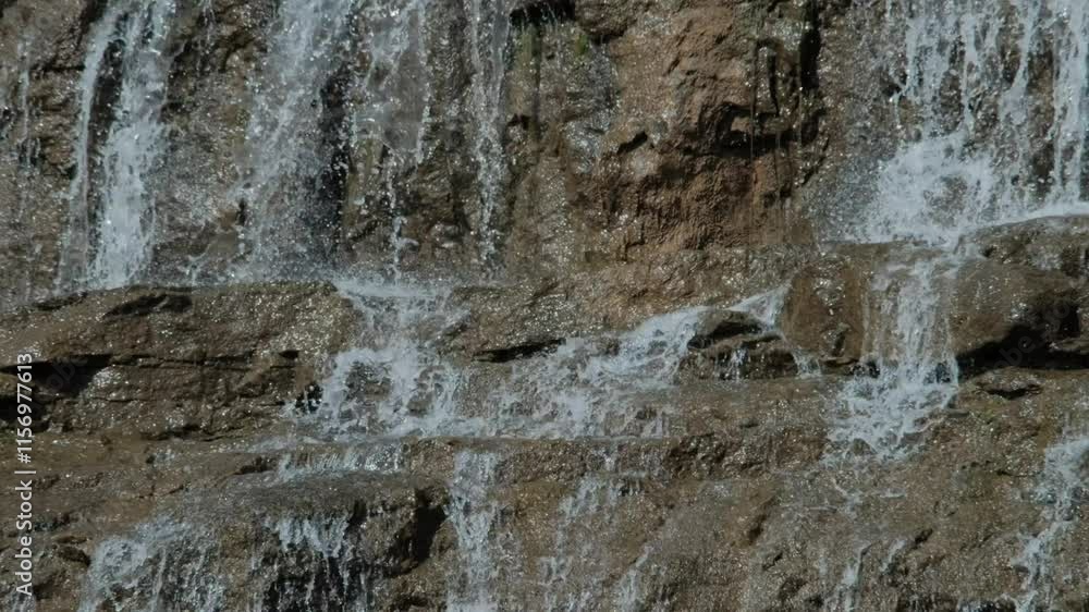 A handheld mid close long shot of water flowing down a waterfall through rocks