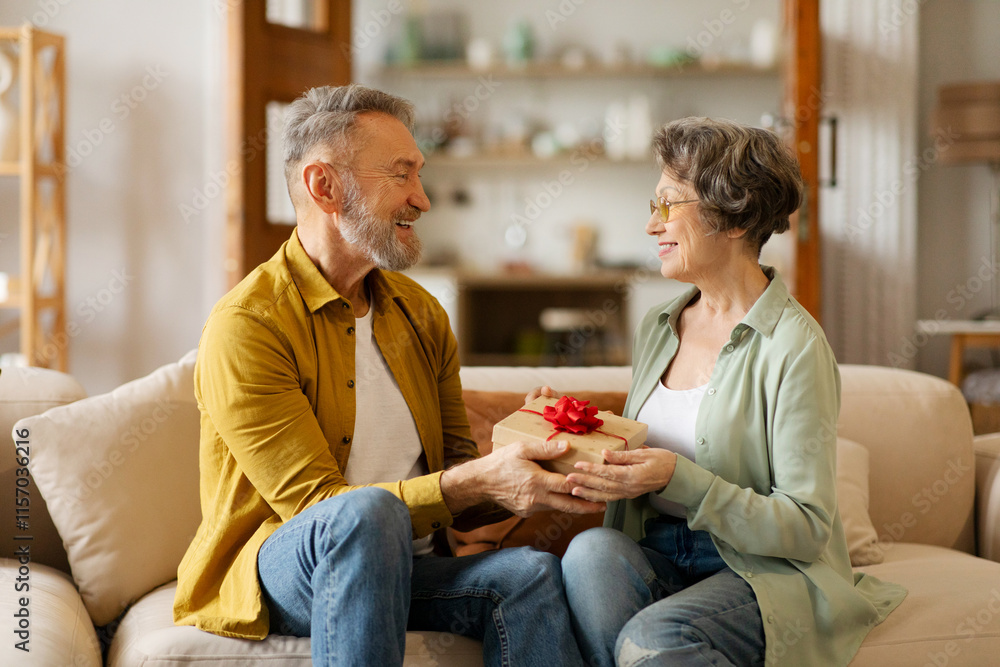 Loving senior man greeting his wife with Valentines Day, birthday or anniversary, giving her gift box, sitting on sofa at home Loving senior man greeting his wife with Valentines Day, birthday or anniversary, giving her gift box, sitting on sofa at home