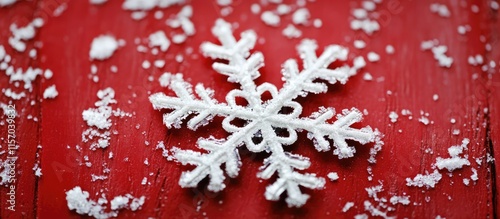 Snowflake resting on a vibrant red surface with scattered snow, showcasing winter beauty and seasonal charm in a close-up view. photo