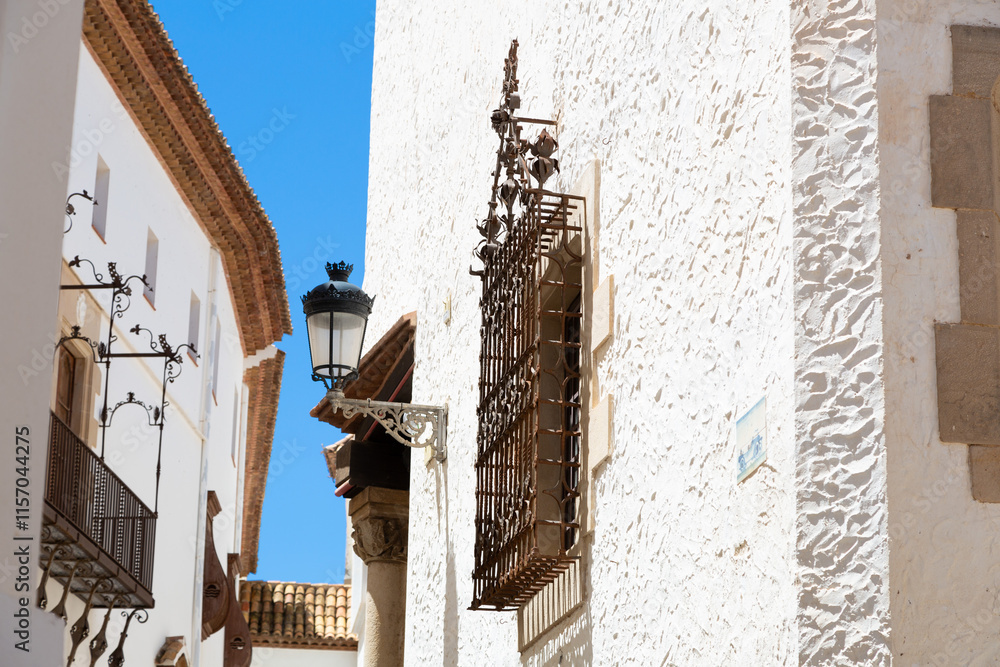Delivery man riding a scooter in a narrow street with white houses in sitges, spain