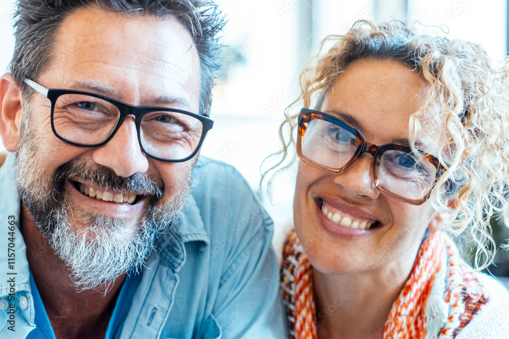 © simona - An adult couple in their late 40s, wearing glasses, smiling and embracing each other with joy while looking at the camera, enjoying a positive moment of their married life, filled with love and happy