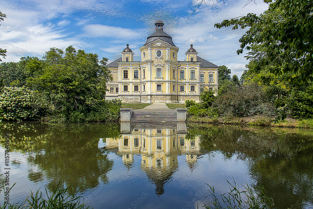 Beautiful castle building. A garden pond in the castle garden with the reflection of the castle building on the water surface. Trees, grass, blue sky with white clouds. Beautiful castle building. A garden pond in the castle garden with the reflection of the castle building on the water surface. Trees, grass, blue sky with white clouds.