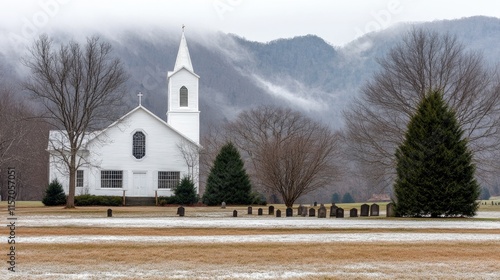 On a foggy morning in West Virginia, an old cemetery stands in front of a small white church amidst the serene mountain backdrop