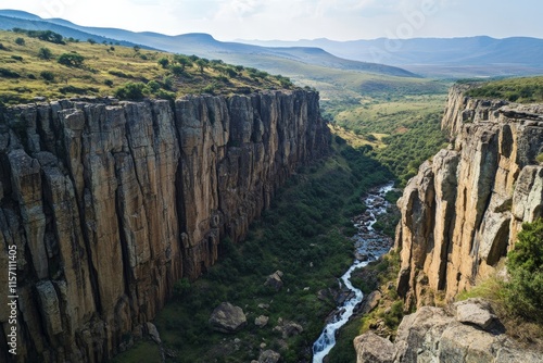 A breathtaking canyon with steep rock formations and a verdant river flowing through, set against a backdrop of rolling hills under a clear, sunlit sky. photo