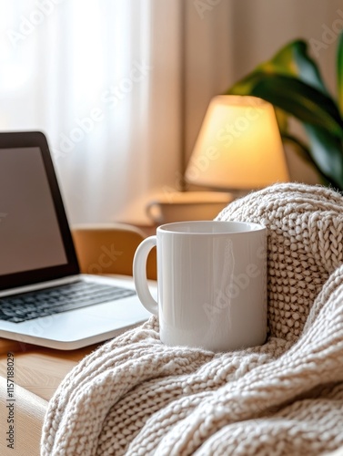 Blank mug mockup photo with a white coffee mug set on a cozy textured knit blanket, accompanied by a laptop and warm ambient lighting.