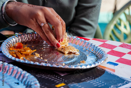 A woman is taking a piece of paratha and pickle from a plate at a roadside dhaba restaurant. The interaction with the food emphasizes the simplicity of the meal. photo