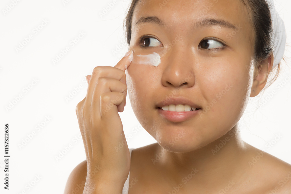 Beautiful young Asian woman applying cosmetic cream treatment on her face