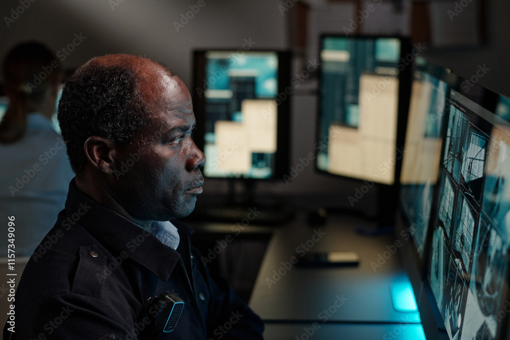 Fototapeta premium Mature African American security guard concentrating on watching cctv video on computer screen in surveillance room