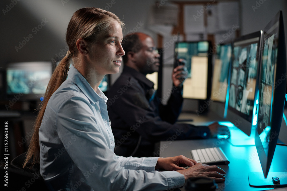 Fototapeta premium Young serious woman in uniform of security officer clicking mouse and looking at desktop computer screen with cctv video
