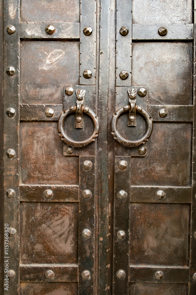Rustic wooden doors with metal accents and large knockers in an ancient style located in a historic building Rustic wooden doors with metal accents and large knockers in an ancient style located in a historic building