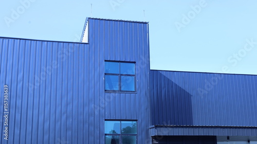 Modern minimalist geometric facade background. Warehouse building exterior metal sheet with light and shadow on surface against blue sky background in low angle with selective focus.