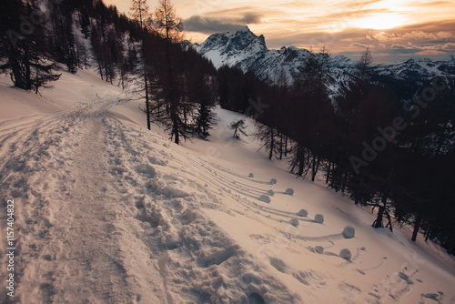 Dramatic colors effect of winter panorama of Mount Civetta at sunset with sunlit clouds seen from a path, with curious snowballs rolled the slope. Fiorentina Valley, Dolomites, Italy