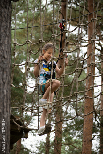 A child navigates a challenging ropes course, showing determination and focus while surrounded by tall trees in a lush outdoor setting.