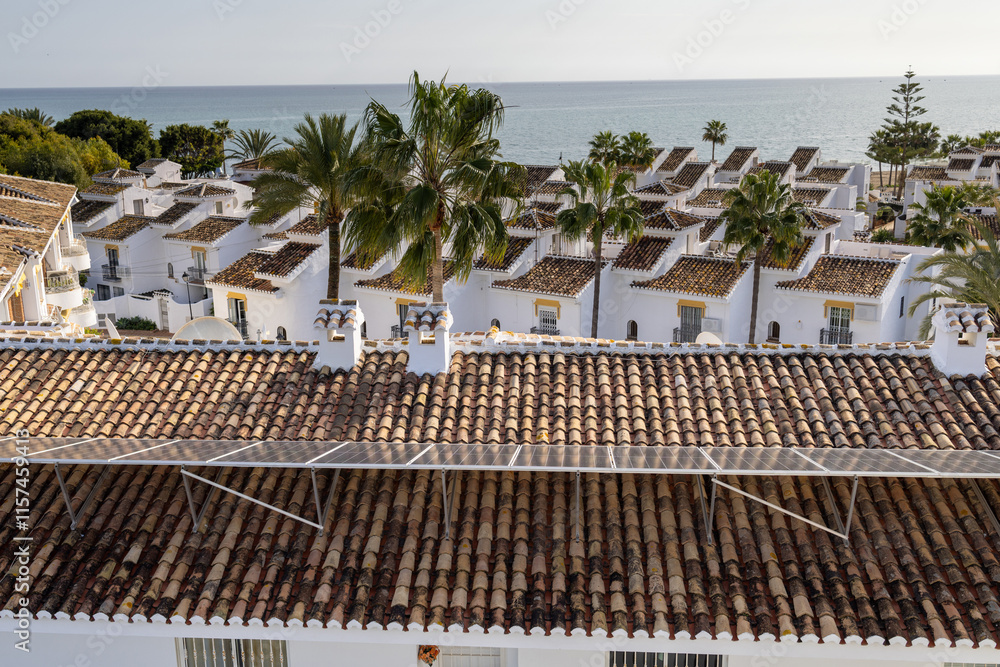 Photo of a typical Spanish apartment block and houses showing the renewable energy from Solar panels on top of the roof with palm trees and the ocean in the town of La Cala de Mijas in Spain