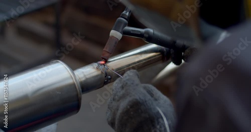 Close up tig welding.Car pipe welding.Automotive exhaust pipe welding with wire filling.The hand of a mechanic or welder is fixing a car exhaust system.Tig welding makes the welds come out beautiful.