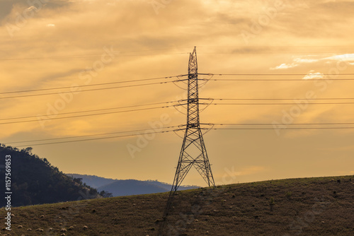 Photograph of a large electricity Transmission Tower on a grassy hill against an orange sunset sky in regional Australia.