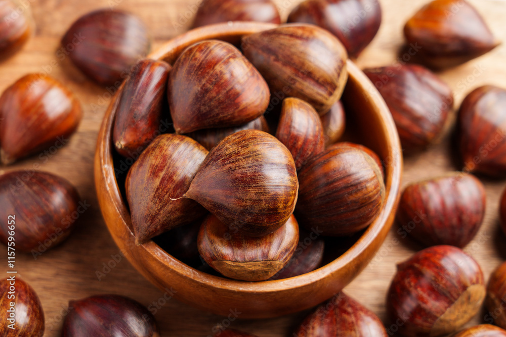 Wooden bowl with fresh harvested chestnuts and scattered organic nuts on rustic table. Wooden bowl with fresh harvested chestnuts and scattered organic nuts on rustic table.