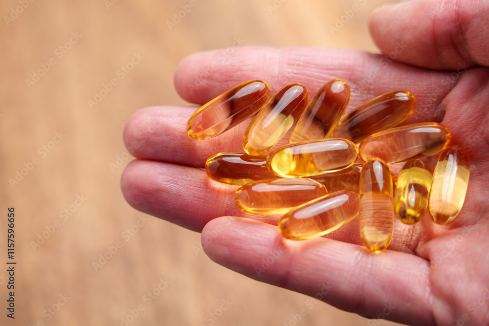Translucent Omega-3 capsules in hand with dry wrinkled skin on a natural wooden background. Healthy supplement Translucent Omega-3 capsules in hand with dry wrinkled skin on a natural wooden background. Healthy supplement
