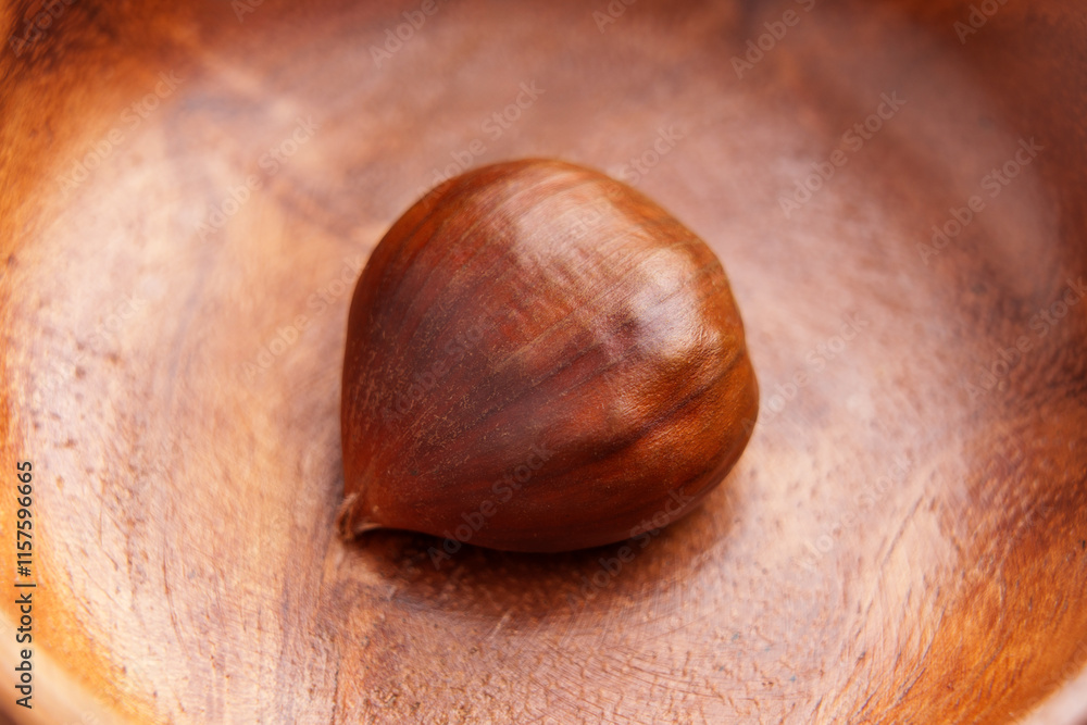Obraz premium A single chestnut in smooth wooden bowl. Brown nut surface on textured grainy wood. Close up