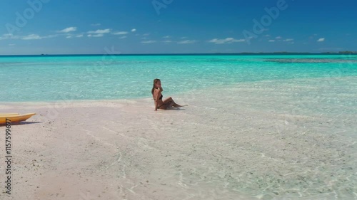 Woman is enjoying the tranquility of a secluded beach, with crystal-clear turquoise water gently lapping at the shore and a kayak resting on the pristine sand
