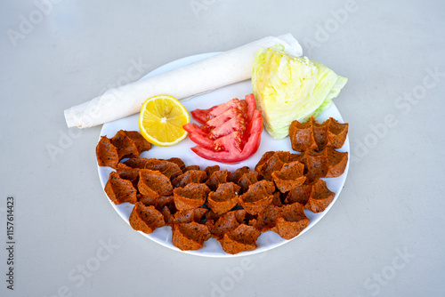 Cig kofte (raw meatball) with lettuce, tomato, pickle and lemon, hot Chee kofta. Turkish local raw food concept.Table scene of assorted take out or delivery foods. Doritoslu duble cig kofte durum. photo