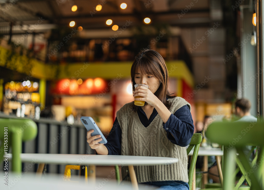 Fototapeta premium Young woman using smartphone and drinking juice in london cafe