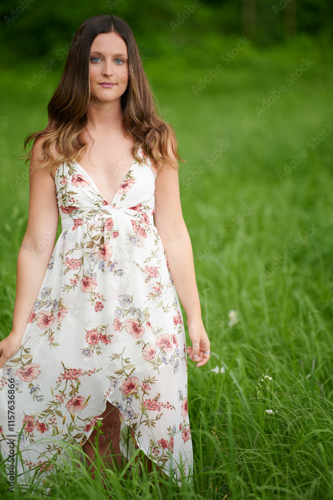 Beautiful young brunette woman in floral print dress walks through tall grass on a summer afternoon Beautiful young brunette woman in floral print dress walks through tall grass on a summer afternoon