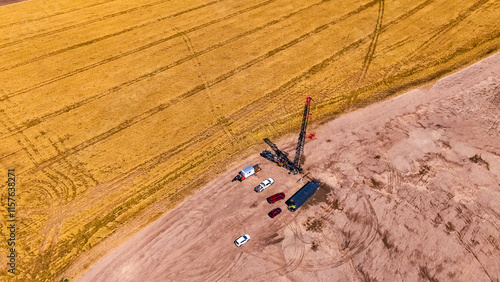 Industrial company producing oil or gas working in the field. Top perspective on the derrick and a few cars beside it near the ripe plantation of wheat. photo