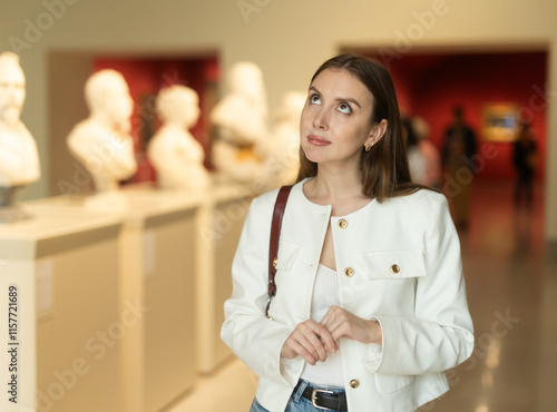 Thoughtful young woman in the sculpture hall at the exhibition. Student studies the history of art in a museum. Woman against the background of sculptural busts