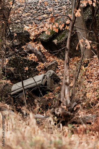 A chair is lying on the ground in a forest. The chair is upside down and has a pile of leaves on it. Scene is eerie and mysterious