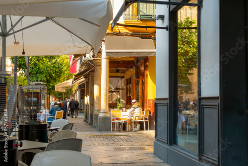 A sidewalk full of shops and sidewalk cafes in the historic Barrio Santa Cruz old town district of the Andalusian city of Seville, Spain. photo