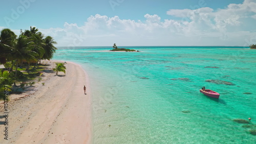 Aerial view of a tourist walking along a beautiful pink sand beach on a tropical island in aitutaki, cook islands, with a small boat anchored in turquoise water