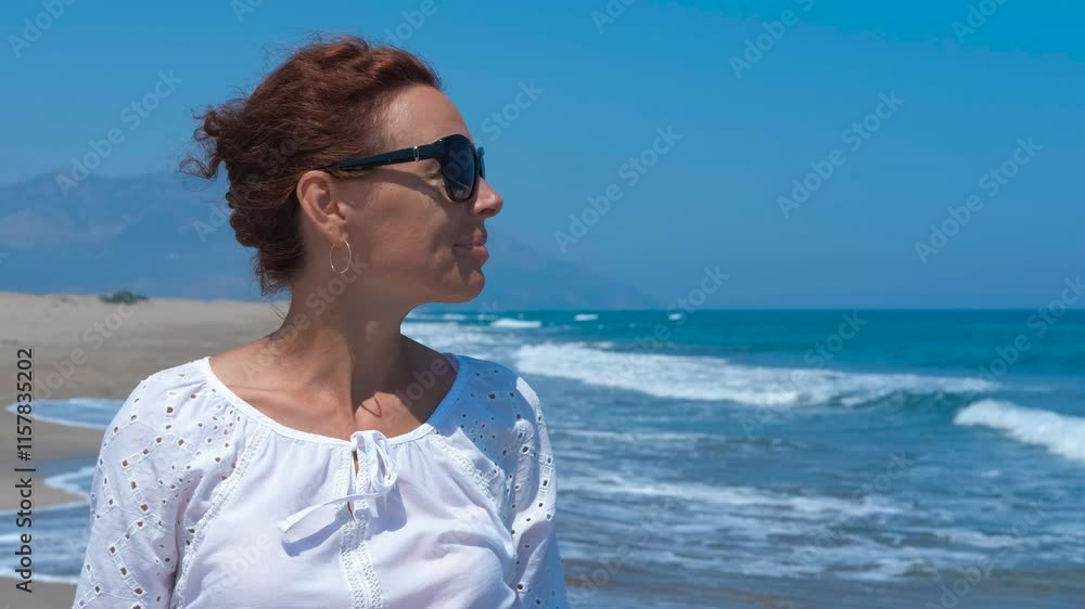Woman enjoying sun and relaxing on beach. Woman wearing sunglasses and a white shirt is enjoying the sun and relaxing on the beach. She is turning her head and smiling Woman enjoying sun and relaxing on beach. Woman wearing sunglasses and a white shirt is enjoying the sun and relaxing on the beach. She is turning her head and smiling
