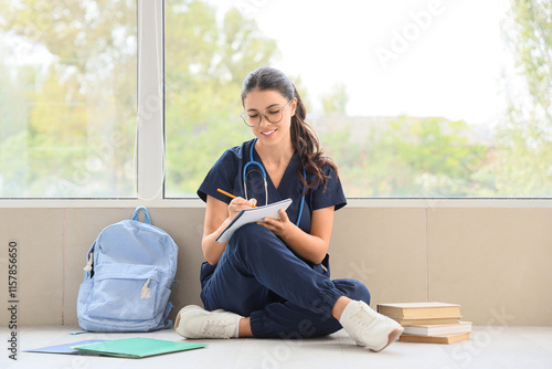 Young female medical student with books and backpack sitting near window in clinic