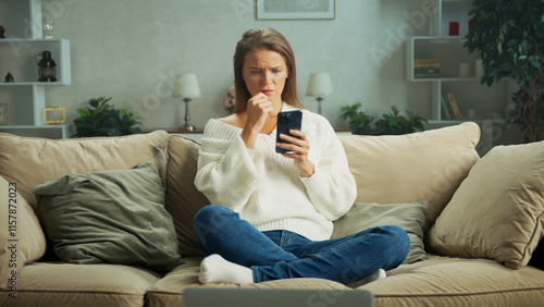 Fotografie Young woman sitting on a cozy sofa at home, looking concerned while reading a me