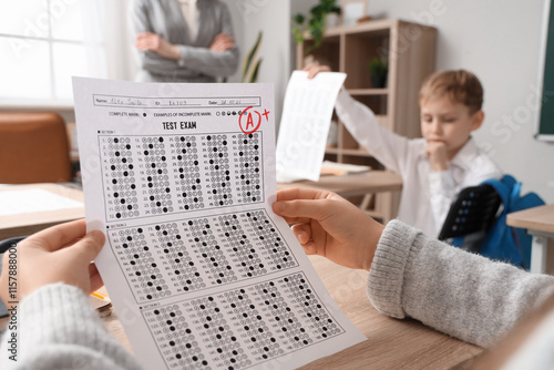 Schoolgirl with results of test at desk in classroom, closeup photo