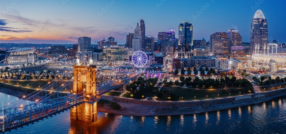 Fototapeta premium Cincinnati skyline at twilight, illuminated by city lights reflecting on the river. Iconic Roebling Suspension Bridge. Evening city views. Downtown, Cincinnati, Ohio, United States