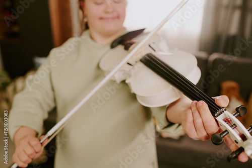 Medium closeup of Caucasian girl with Down syndrome practicing violin, standing in living room at home photo