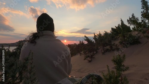 Back view of woman with a blanket on a sand beach looking at the sunset on the sea