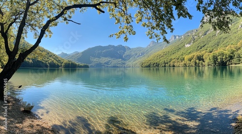 Fototapeta Naklejka Na Ścianę i Meble -  Serene mountain lake with crystal-clear water, tree branches framing a picturesque view on a sunny day.