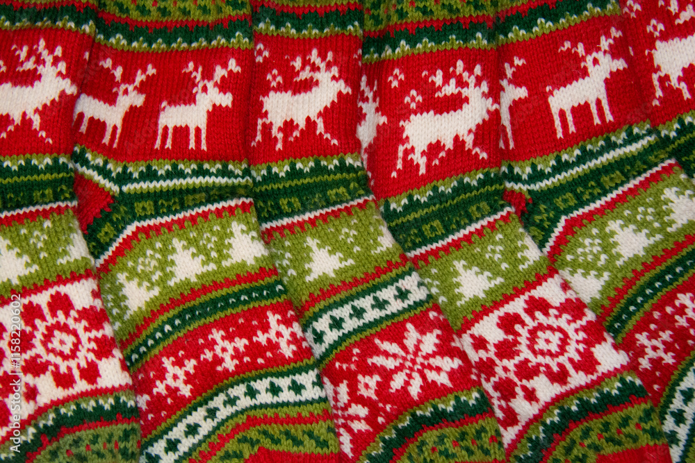 Beautiful New Year's socks, knitted from woolen yarn in red, white and green colors, with a pattern of deer, snowflakes, Christmas trees and flowers lie in a row Beautiful New Year's socks, knitted from woolen yarn in red, white and green colors, with a pattern of deer, snowflakes, Christmas trees and flowers lie in a row