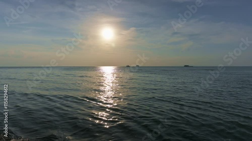 Ripples gently crashing to the shore in the evening under sunlight with cloudy blue sky. Tranquil scene of the sea before sunset.