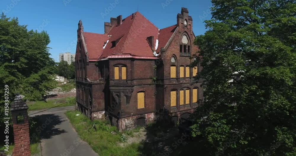 Old, abandoned brick tenement building with boarded-up windows, surrounded by a wall and green trees on a sunny summer day, dynamic 4K drone shot Old, abandoned brick tenement building with boarded-up windows, surrounded by a wall and green trees on a sunny summer day, dynamic 4K drone shot