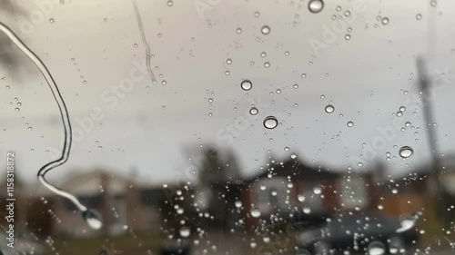 A video of rain with water flowing on a glass, blurring the view of a house